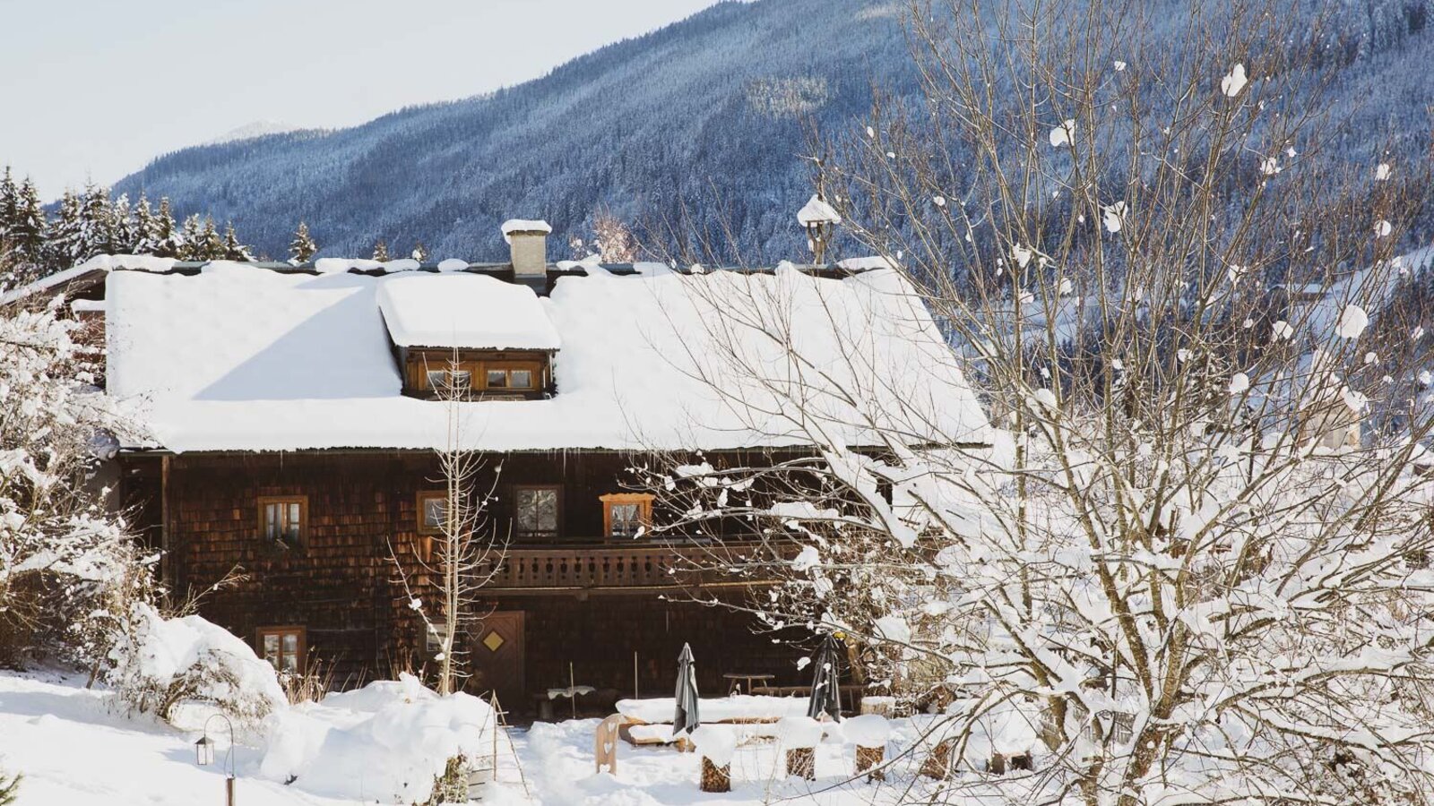 The holiday home in winter, with a snow-covered roof, wooden balcony, and an outdoor seating area.
