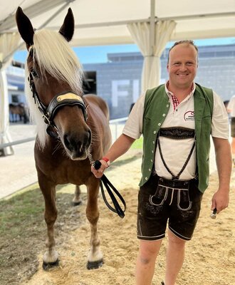 A friendly host in traditional attire presents a beautiful horse from the farmhouse.