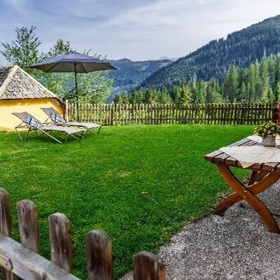 The farmhouse's inviting garden with a manicured lawn, sun loungers, and a cozy wooden seating area overlooking the mountains.