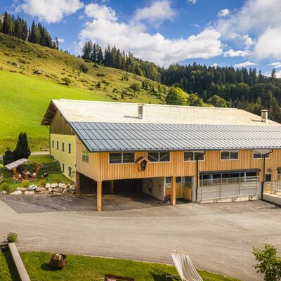The farmhouse's traditional building surrounded by lush green meadows and forested hills.