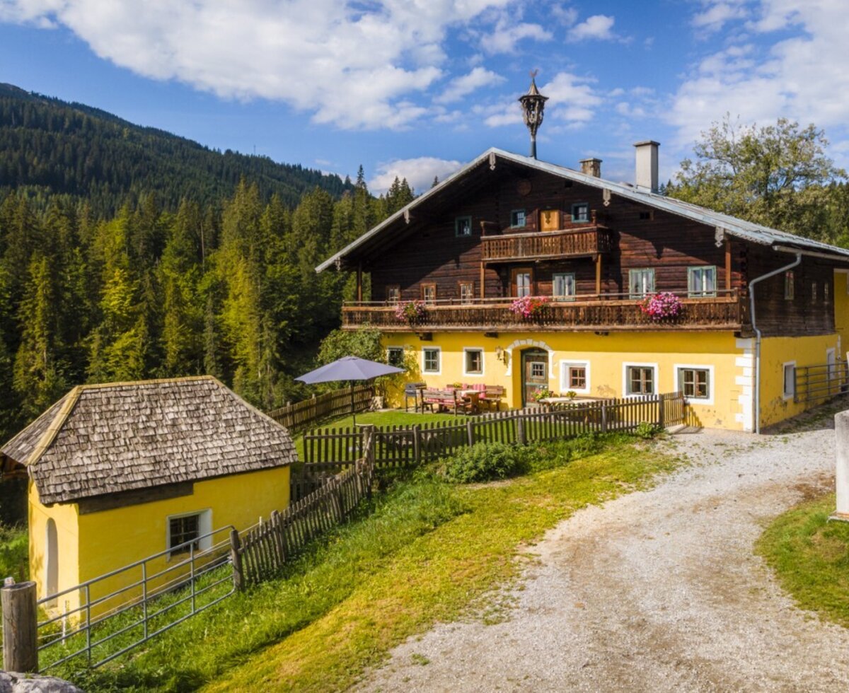 The historic farmhouse featuring charming wooden balconies, beautifully nestled against a backdrop of lush forests.
