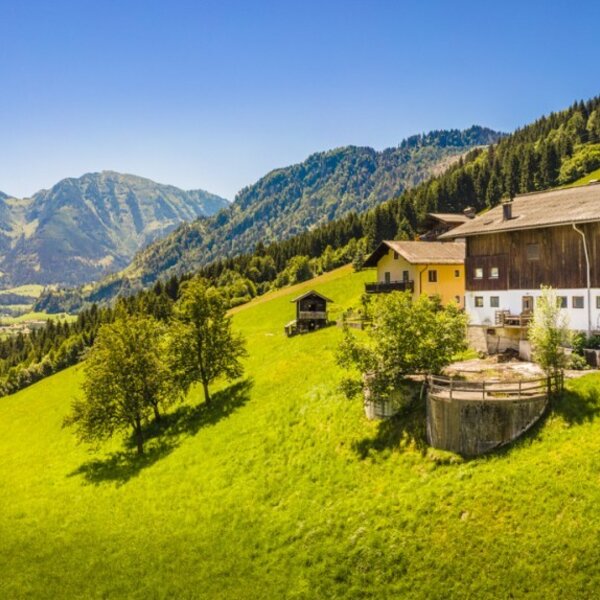 Farmhouse located on a green hillside, offering views of a village and surrounding mountains.