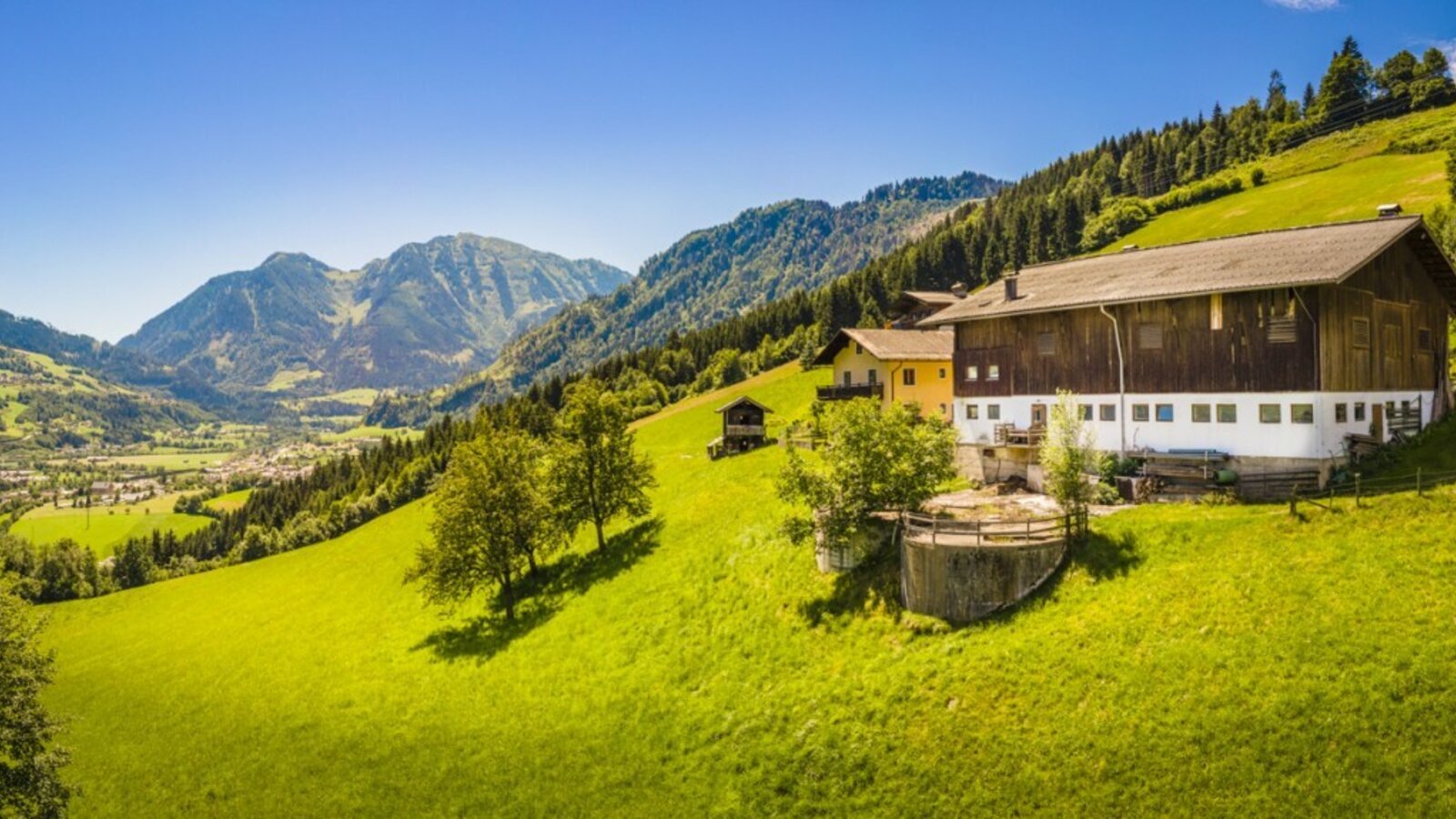 Farmhouse located on a green hillside, offering views of a village and surrounding mountains.
