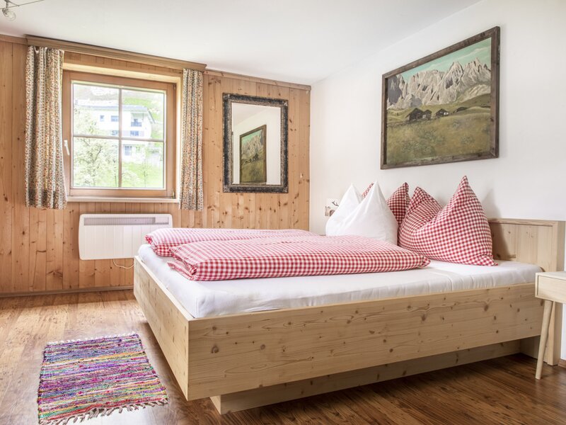 Double bedroom in the farmhouse featuring a wooden bed, wood-paneled walls, a window, and a landscape painting.
