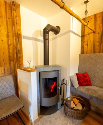 Modern wood-burning stove with burning fire, wood basket, and seating in the Bed and Breakfast.