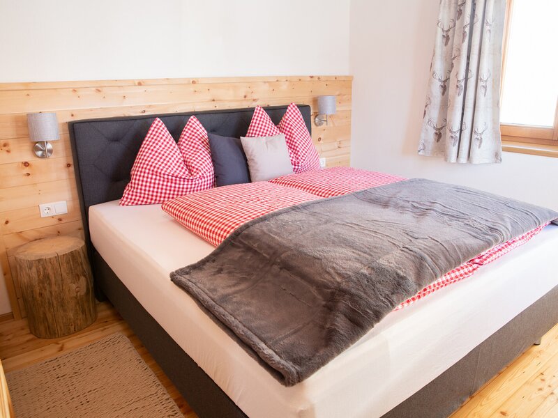 Double bedroom in the farm house featuring a wooden headboard, red and white checkered bedding, and a tree stump bedside table.