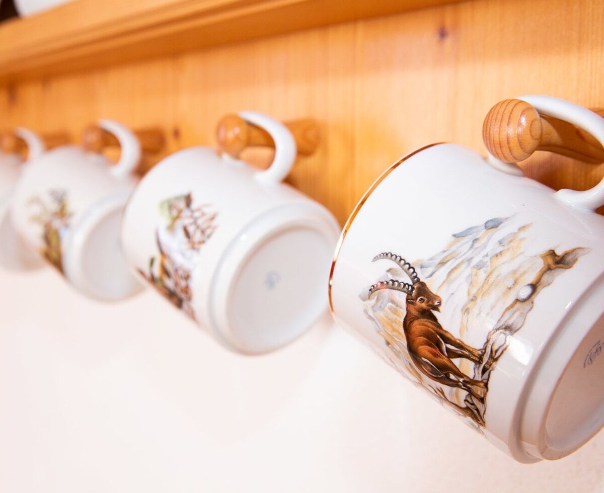 Kitchen mugs featuring animal designs and wooden handles, displayed on a wooden rack in the Farm House.