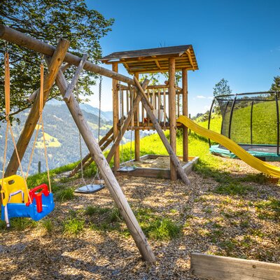The farmhouse provides an outdoor children's play area with a swing set, a wooden play structure including a slide and sandpit, and a trampoline.