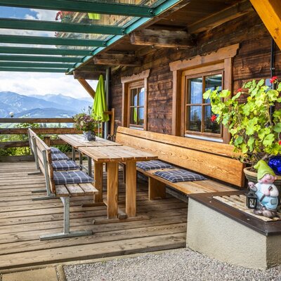 Covered wooden terrace at the Alpine Hut with outdoor dining furniture and mountain views.