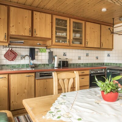 The kitchen in the Bed and Breakfast features wooden cabinets, a sink, coffee maker, toaster, dishwasher, oven, and a traditional wood-burning stove, along with a dining table.