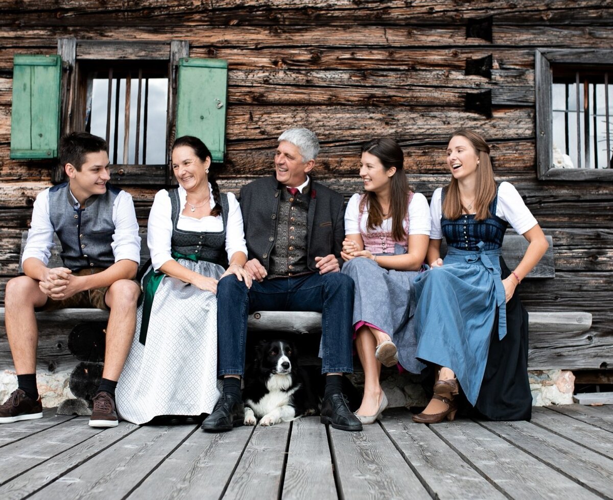 The family Vitzthum sits with their dog on a wooden bench in front of the farmhouse.