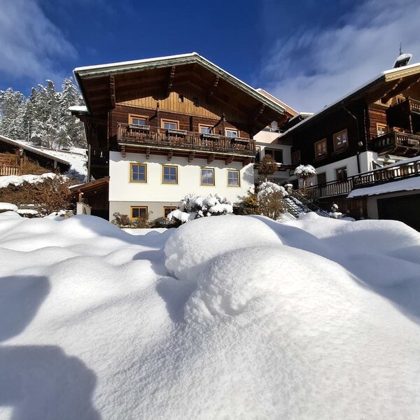 The multi-story Farm House exterior, featuring wooden balconies and a snow-covered garden during winter.