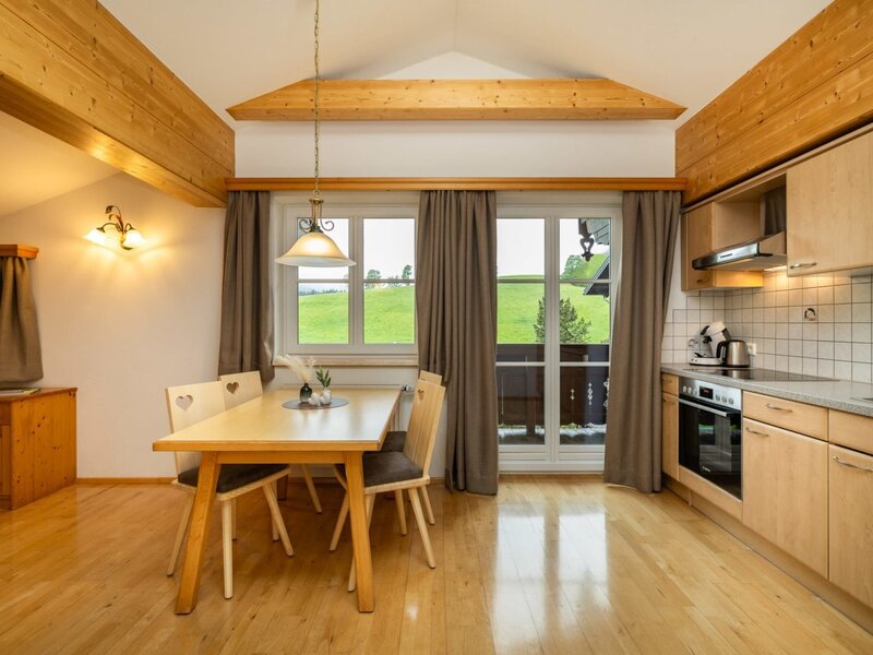 Fully equipped kitchen and dining area in the apartment, featuring a wooden table, modern appliances, and balcony access with nature views.
