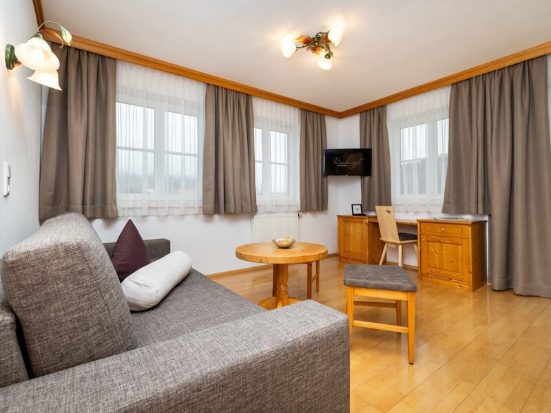 Living area of an apartment on the farmhouse, featuring a sofa, coffee table, desk, TV, and wooden floor.
