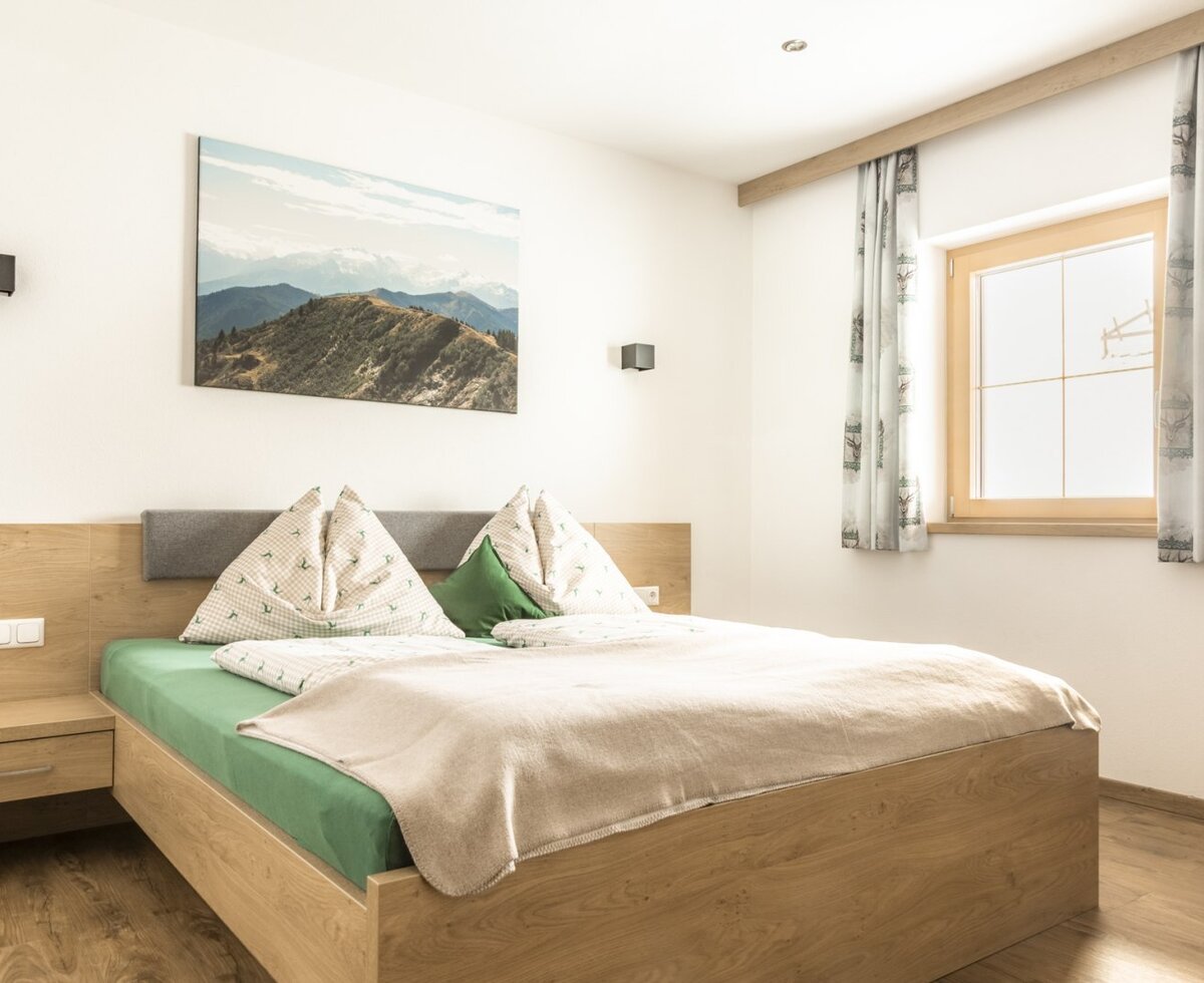 Double bedroom with a wooden bed, nightstand, and window with curtains.