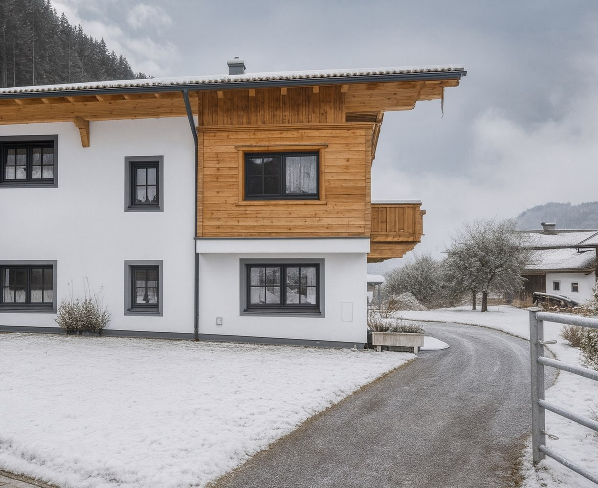 Exterior view of the farmhouse with a white facade, wooden cladding, and balconies, surrounded by snow.