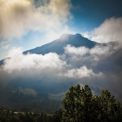 The surrounding mountain landscape with clouds and forested slopes, characteristic of the area near the farmhouse.