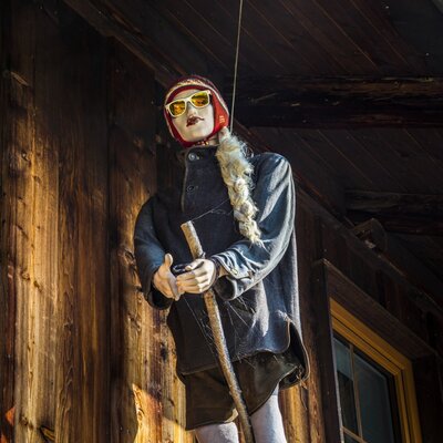 A mannequin wearing old-fashioned ski gear and skis is displayed on the wooden exterior wall of the farm house.