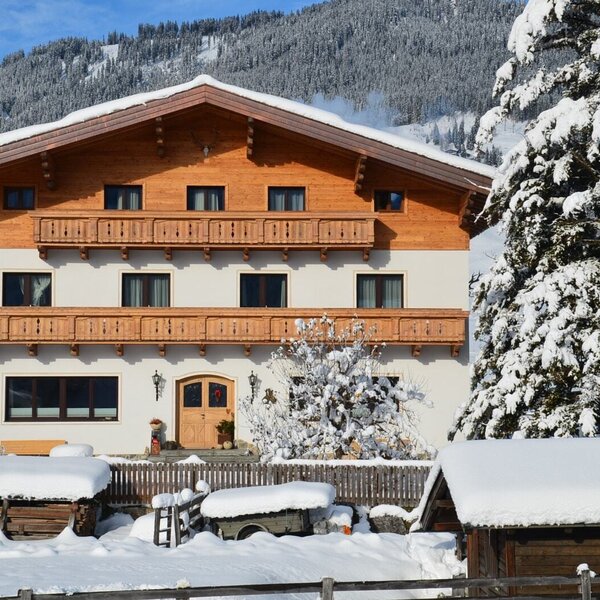 The exterior of the Farm House in winter, featuring wooden balconies and a snow-covered mountain backdrop.