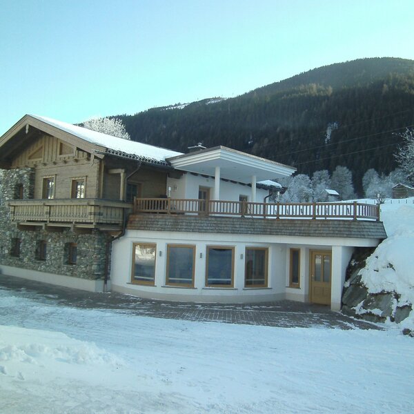 The farm house exterior in winter, built with stone and wood, with snow-covered grounds and a mountain view. The farm house exterior in winter, built with stone and wood, with snow-covered grounds and a mountain view.