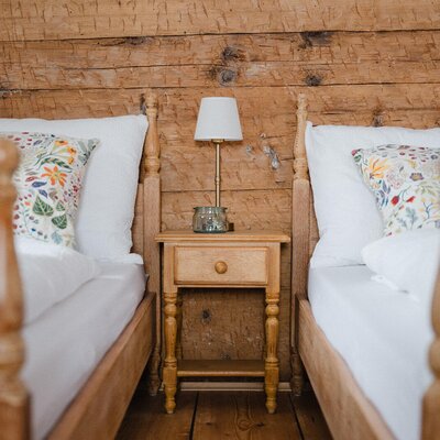 Bedroom in the Bed and Breakfast with two single beds, a wooden wall, and a nightstand with a lamp.