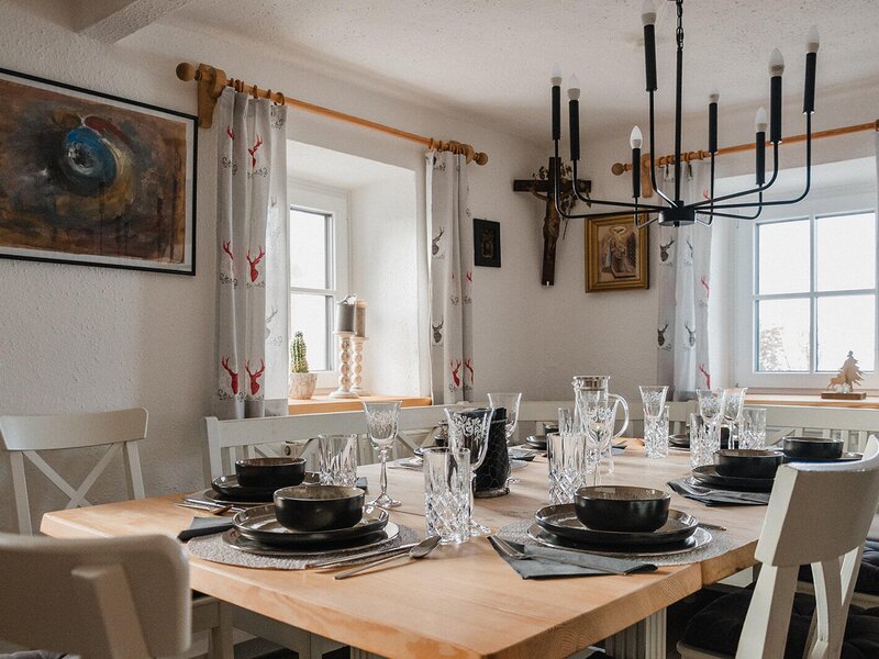 Set dining table for multiple guests in the Bed and Breakfast, surrounded by windows with deer-patterned curtains.