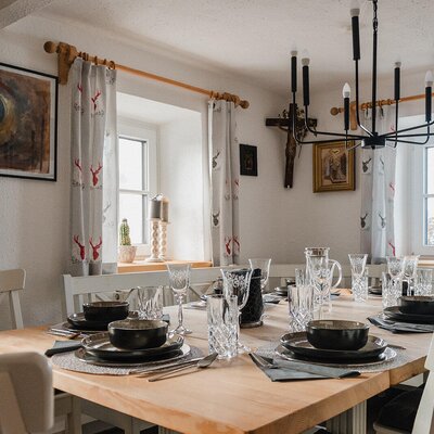 Set dining table for multiple guests in the Bed and Breakfast, surrounded by windows with deer-patterned curtains.