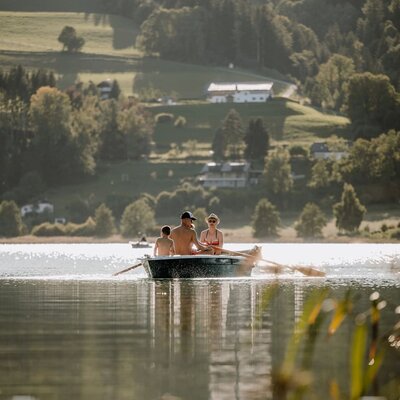 A family rowing on a lake with green hills and houses in the background, an outdoor activity near the Bed and Breakfast.