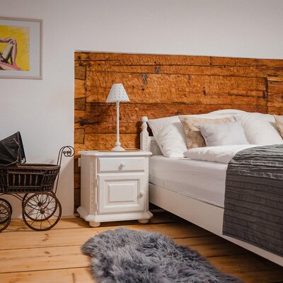 Bedroom in the Bed and Breakfast featuring a double bed, rustic wooden headboard, white nightstand, wooden floor, and a decorative vintage pram.