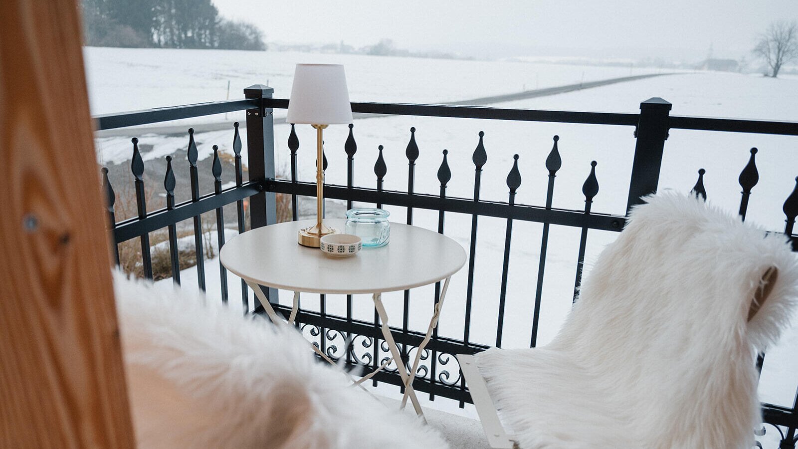 Balcony of the Bed and Breakfast with a table, two faux fur chairs, and a view of a snowy landscape.
