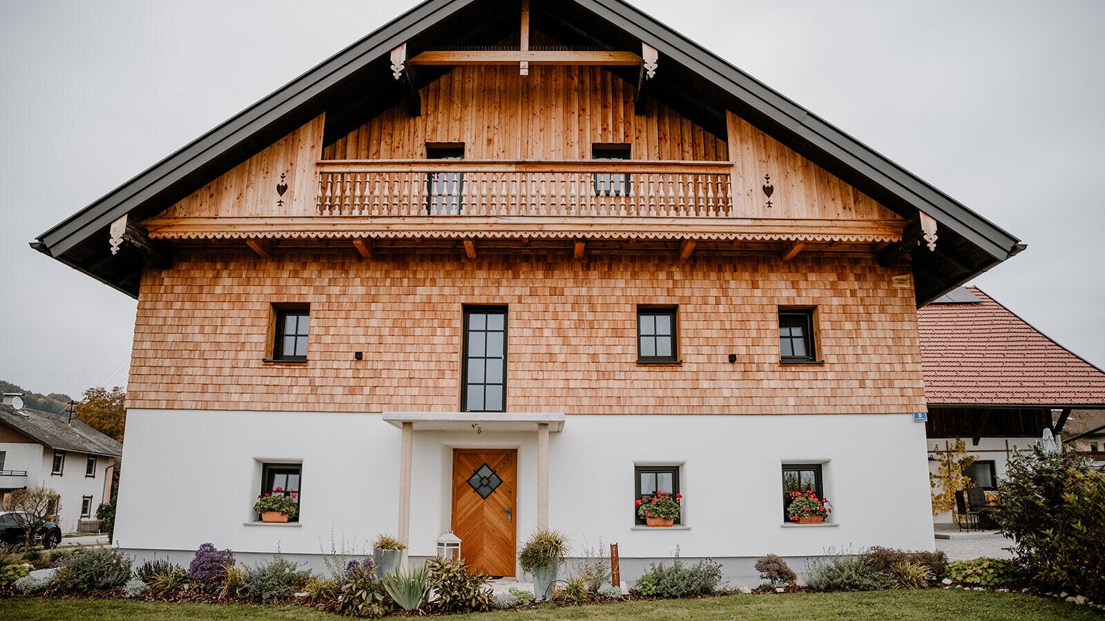 Exterior view of the Bed and Breakfast featuring a wooden facade, white plaster, a balcony, and a front garden.