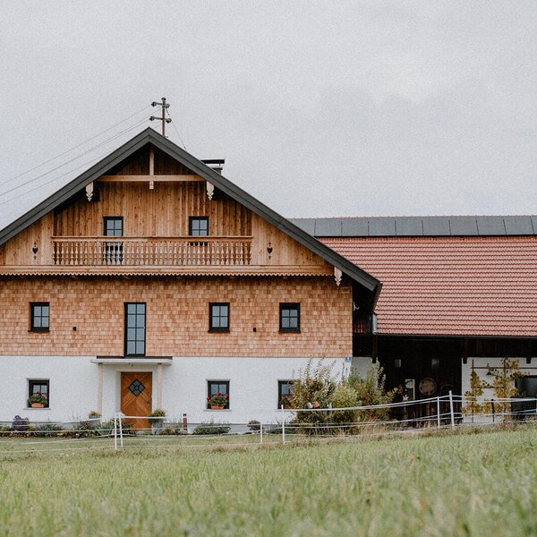 The traditional wooden facade of the restored farmhouse, featuring a balcony and an adjacent building section.