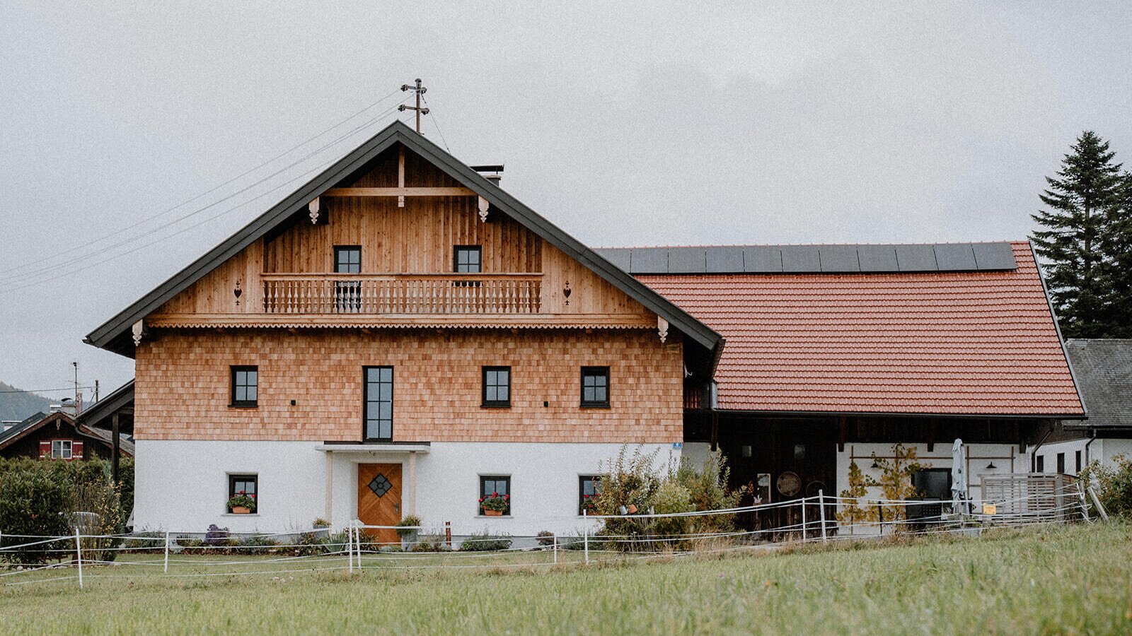 The traditional wooden facade of the restored farmhouse, featuring a balcony and an adjacent building section.