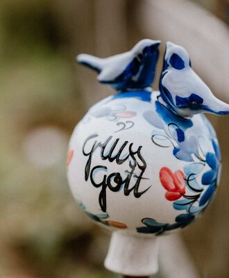 A decorative garden stake with ceramic birds and the inscription 'Gruss Gott' at the farmhouse.