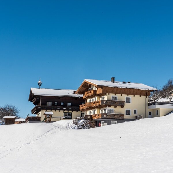The exterior of the farmhouse during winter, set on a snow-covered slope and featuring multiple balconies.