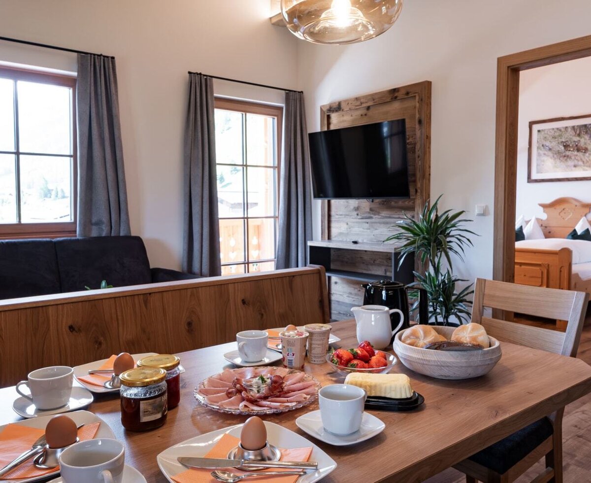 The dining area in the Bauernhof is set for breakfast, offering a view of the living area with a sofa and TV, and an adjoining bedroom.