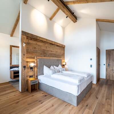 Double bedroom in the Farm House with a wooden accent wall, exposed beams, a double bed, and an adjoining bathroom area.