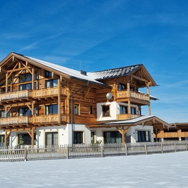 The traditional wooden Farm House exterior, featuring multiple balconies, stands in a snow-covered field.
