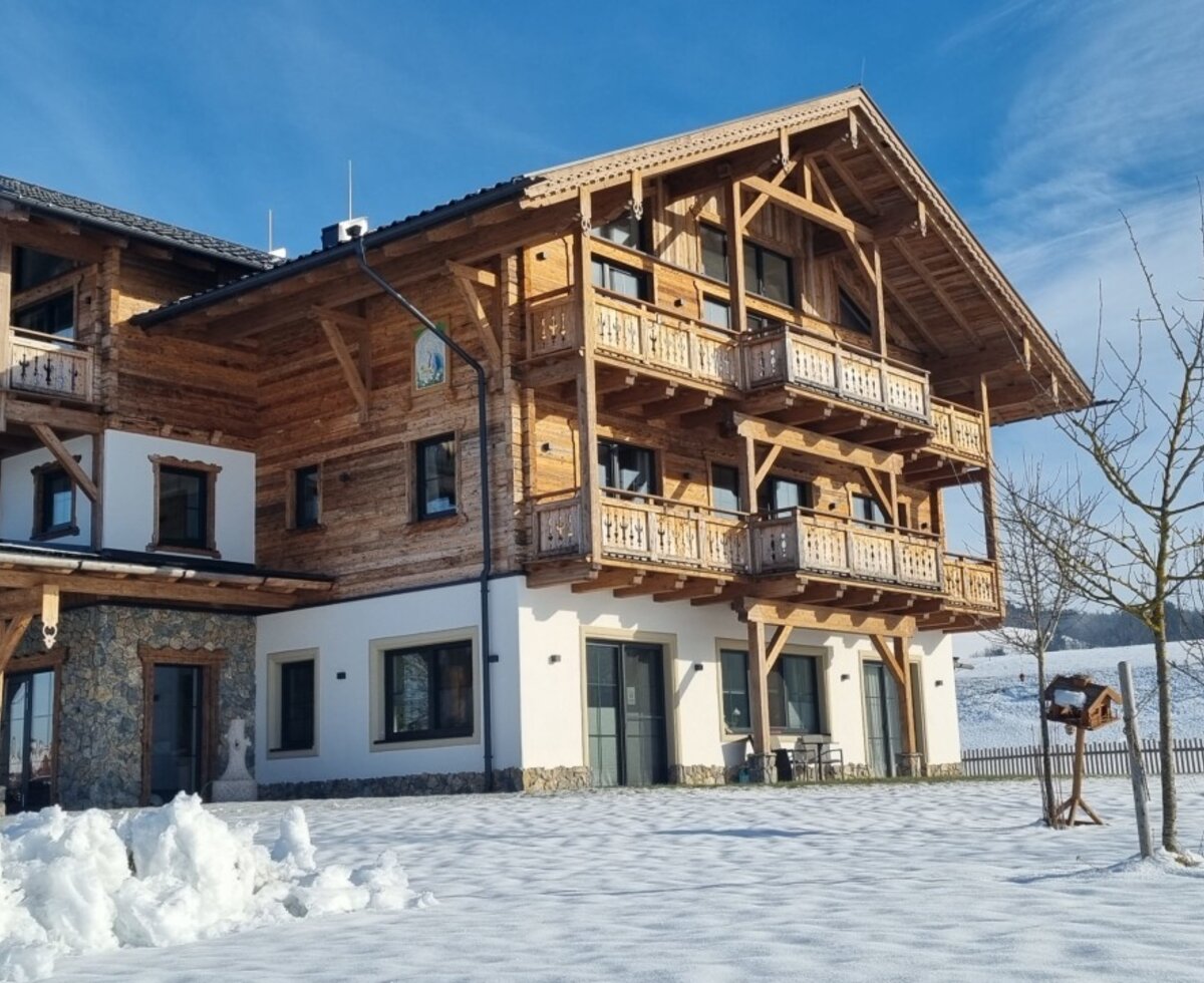 The Farm House exterior in winter, featuring traditional wooden architecture, multiple balconies, and a snowy surrounding.