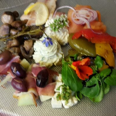 A mixed appetizer plate featuring cured meats, olives, cheeses, marinated mushrooms, bell peppers, and garnished dips.