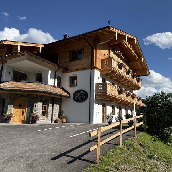 The inviting farmhouse featuring a traditional wooden facade and flower-filled balconies under a bright blue sky.