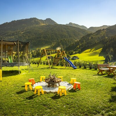 The farmhouse's spacious garden featuring a children's playground, a cozy fire pit area, and scenic mountain views.