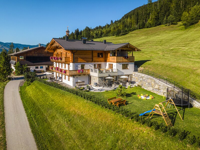 The inviting farmhouse features a spacious green garden with a children's playground and sunny outdoor seating areas.