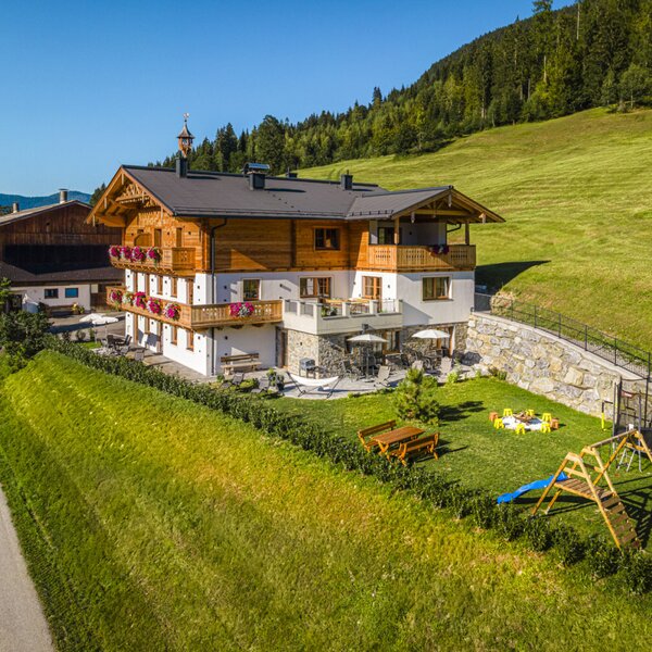 The inviting farmhouse features a spacious green garden with a children's playground and sunny outdoor seating areas.