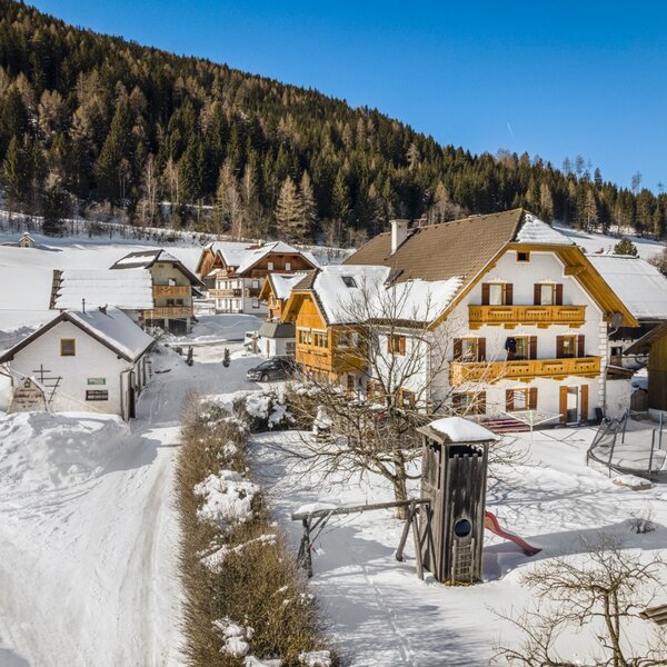 The Farm House with its wooden balconies, surrounded by a snow-covered garden featuring a children's play tower and a trampoline. The Farm House with its wooden balconies, surrounded by a snow-covered garden featuring a children's play tower and a trampoline.