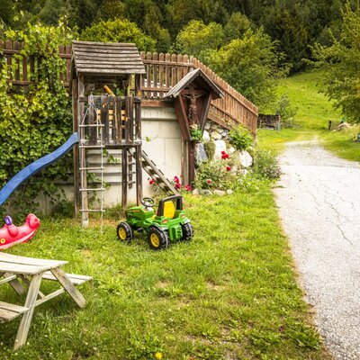 The farmhouse's inviting play area with a slide, toy tractor, and a small wooden picnic table on the grassy lawn.