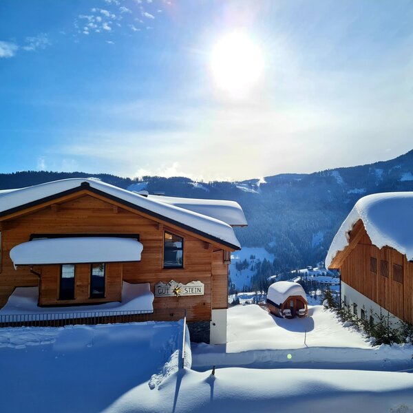 The farm house "GUT STEIN" and adjacent building, both snow-covered, feature a barrel-shaped outdoor structure with a mountain landscape in the background. The farm house "GUT STEIN" and adjacent building, both snow-covered, feature a barrel-shaped outdoor structure with a mountain landscape in the background.