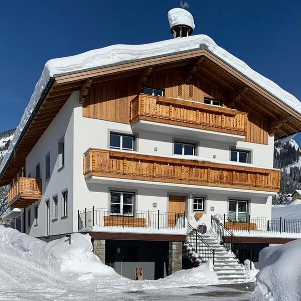 Exterior view of the farmhouse in winter, with a snow-covered roof and wooden balconies.