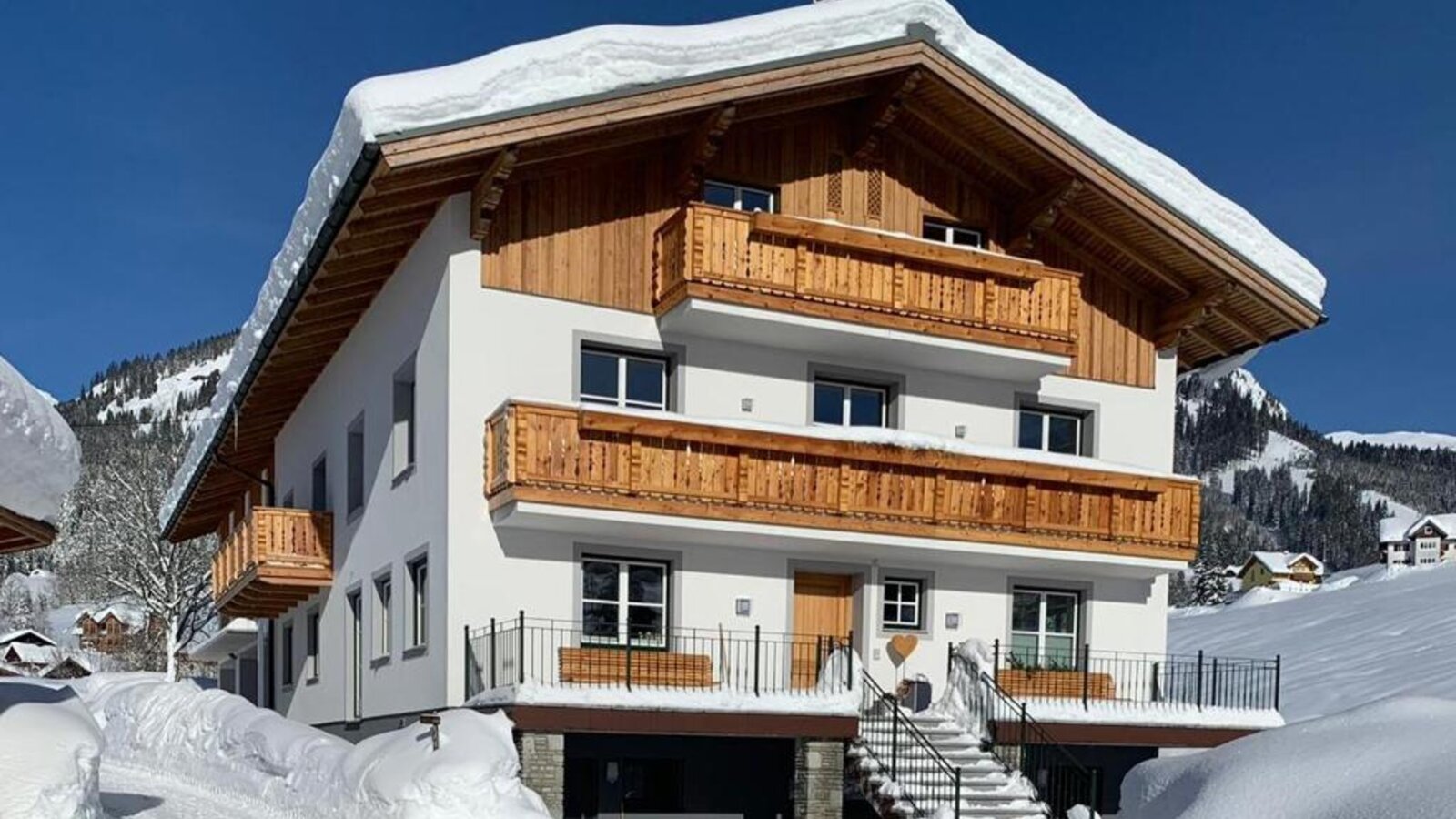 Exterior view of the farmhouse in winter, with a snow-covered roof and wooden balconies.