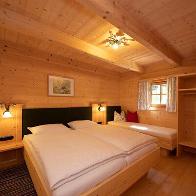 Wood-paneled double bedroom in the farmhouse featuring a tiled stove, an additional single daybed, and a built-in wooden closet.